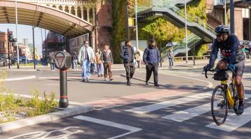 Pedestrians approaching a zebra crossing on a busy urban road with a cyclist is passing